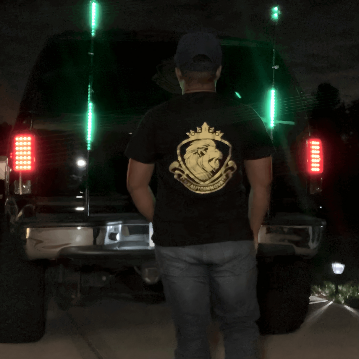 Man wearing LynXautoinnovate logo shirt stands behind truck with green LED lights at night.