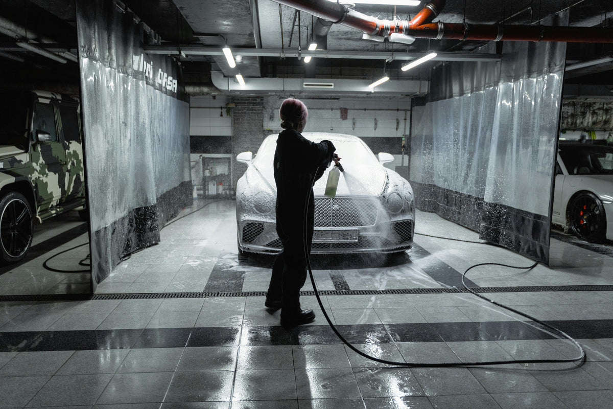 Person detailing luxury car with foam spray in modern garage, LynXautoinnovate automotive parts